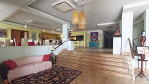 A spacious lobby with a staircase leading to a dining area, a sofa with a patterned rug, and a TV mounted on the wall. - Santana Hotel Restaurante (Palazuelos de Eresma)