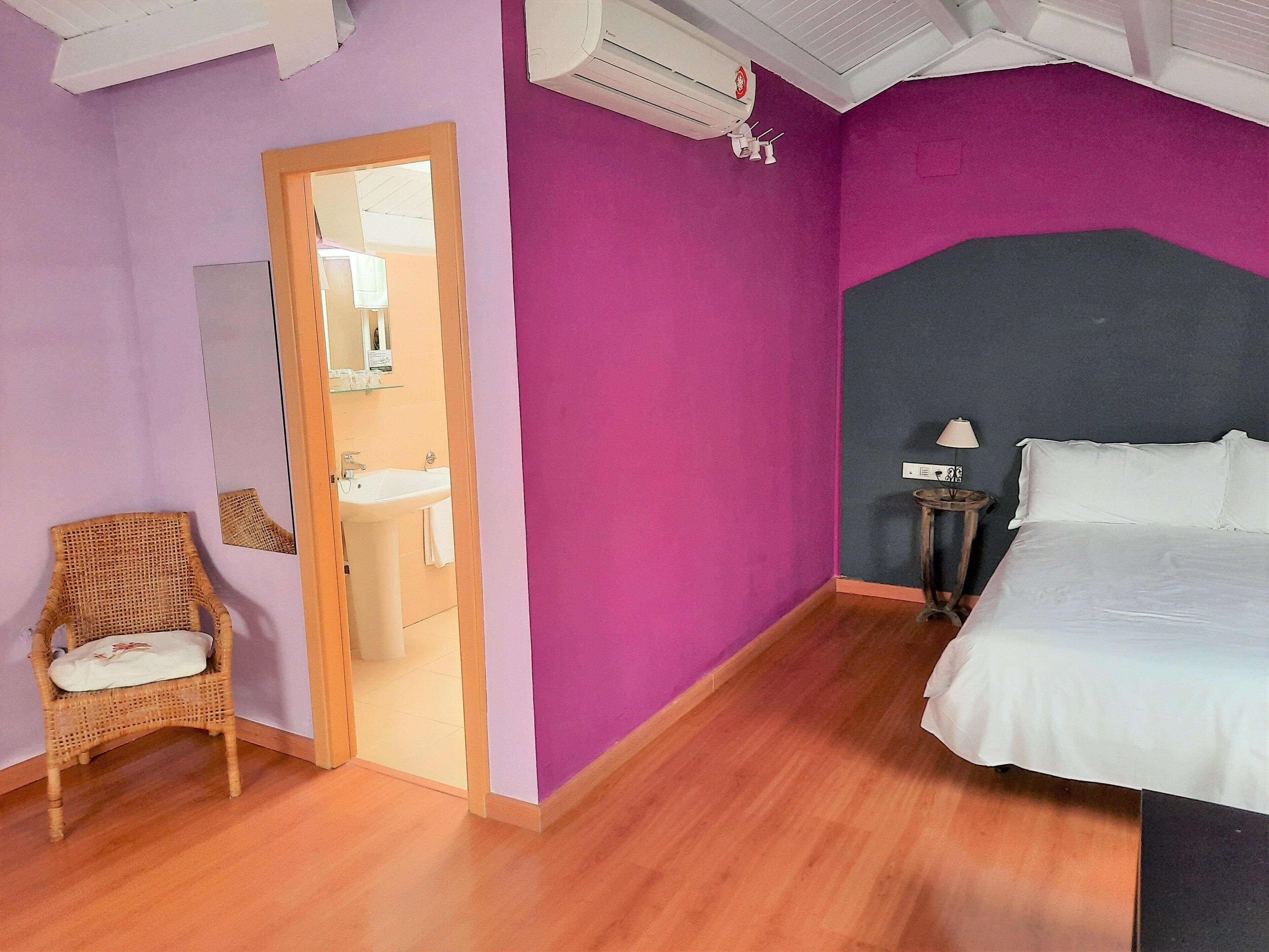 Un dormitorio con cama, una silla, baño con lavamanos y unidad de aire acondicionado.