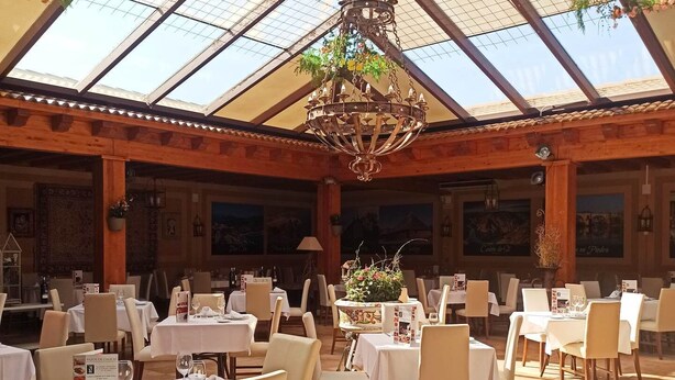 A restaurant with a high ceiling and glass panels, featuring tables set for dining and a chandelier. - Santana Hotel Restaurante (Palazuelos de Eresma)