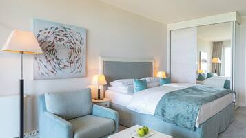 A hotel room with a bed, a chair, a bedside table, a lamp, and a painting on the wall.