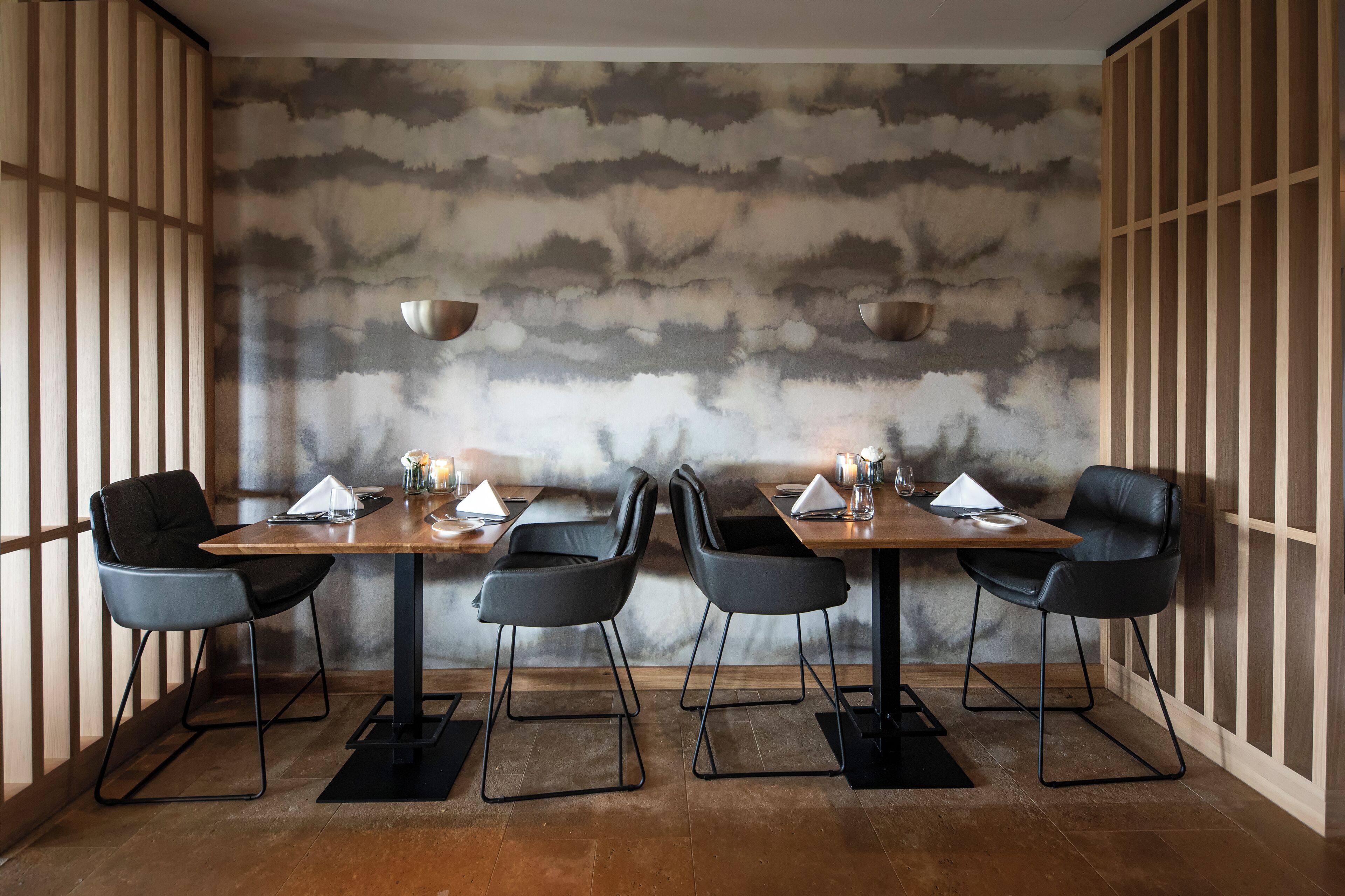 A dining area with a modern design, featuring a wooden table and black chairs, set against a textured wall.