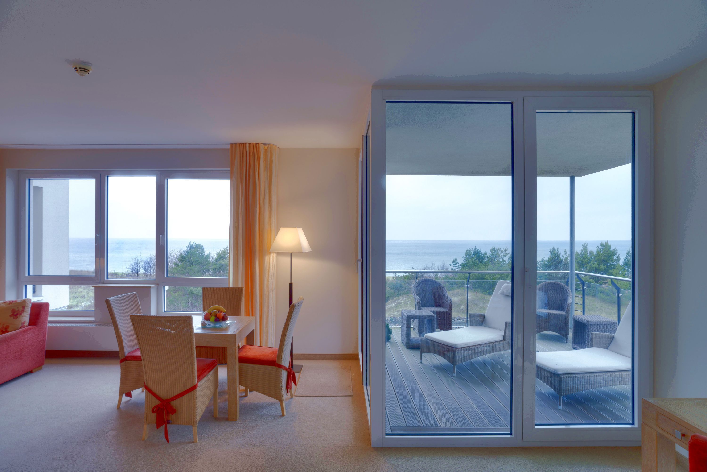 A modern room with a balcony, a dining area, and a view of the sea.