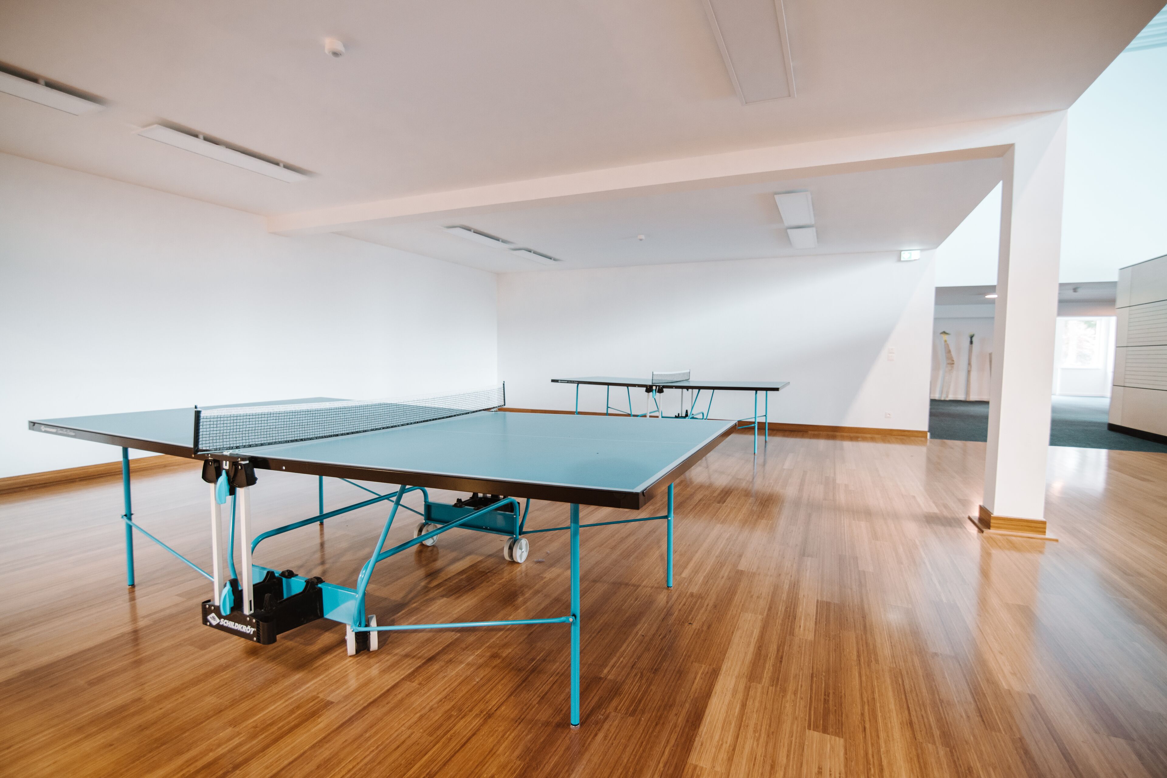 A spacious room with a ping pong table, another table in the background, and a wooden floor.