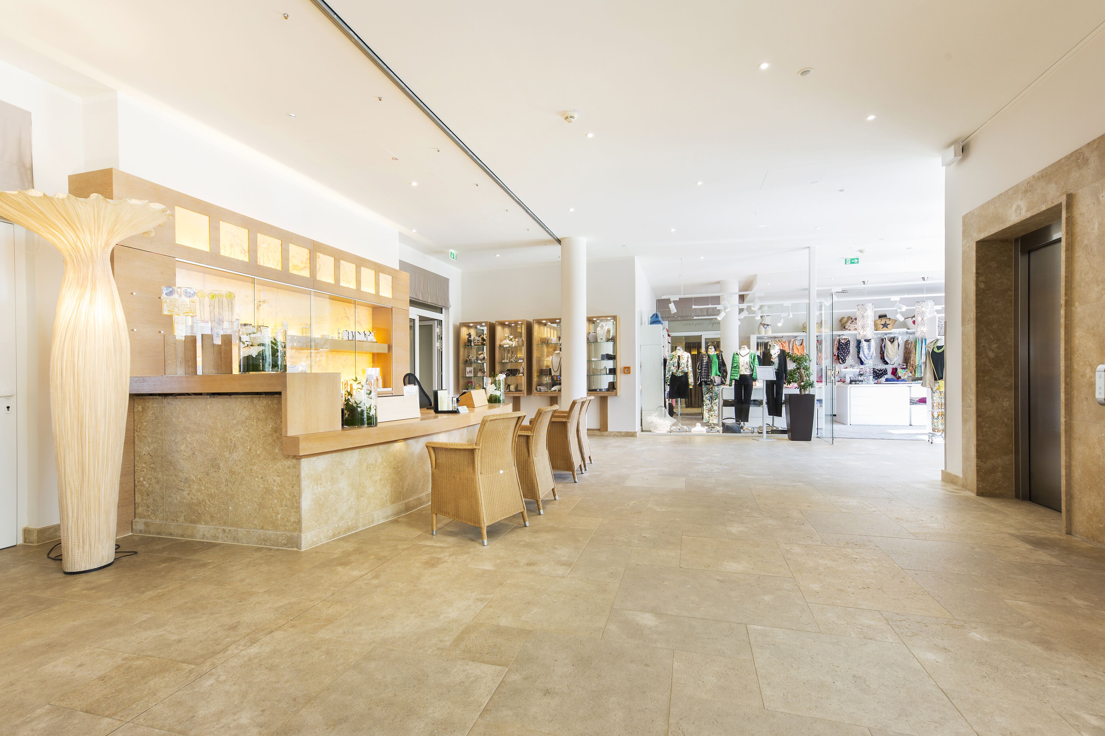 Eine geräumige Lobby mit einer Rezeption, einer Sitzecke und einem Bekleidungsgeschäft im Hintergrund.