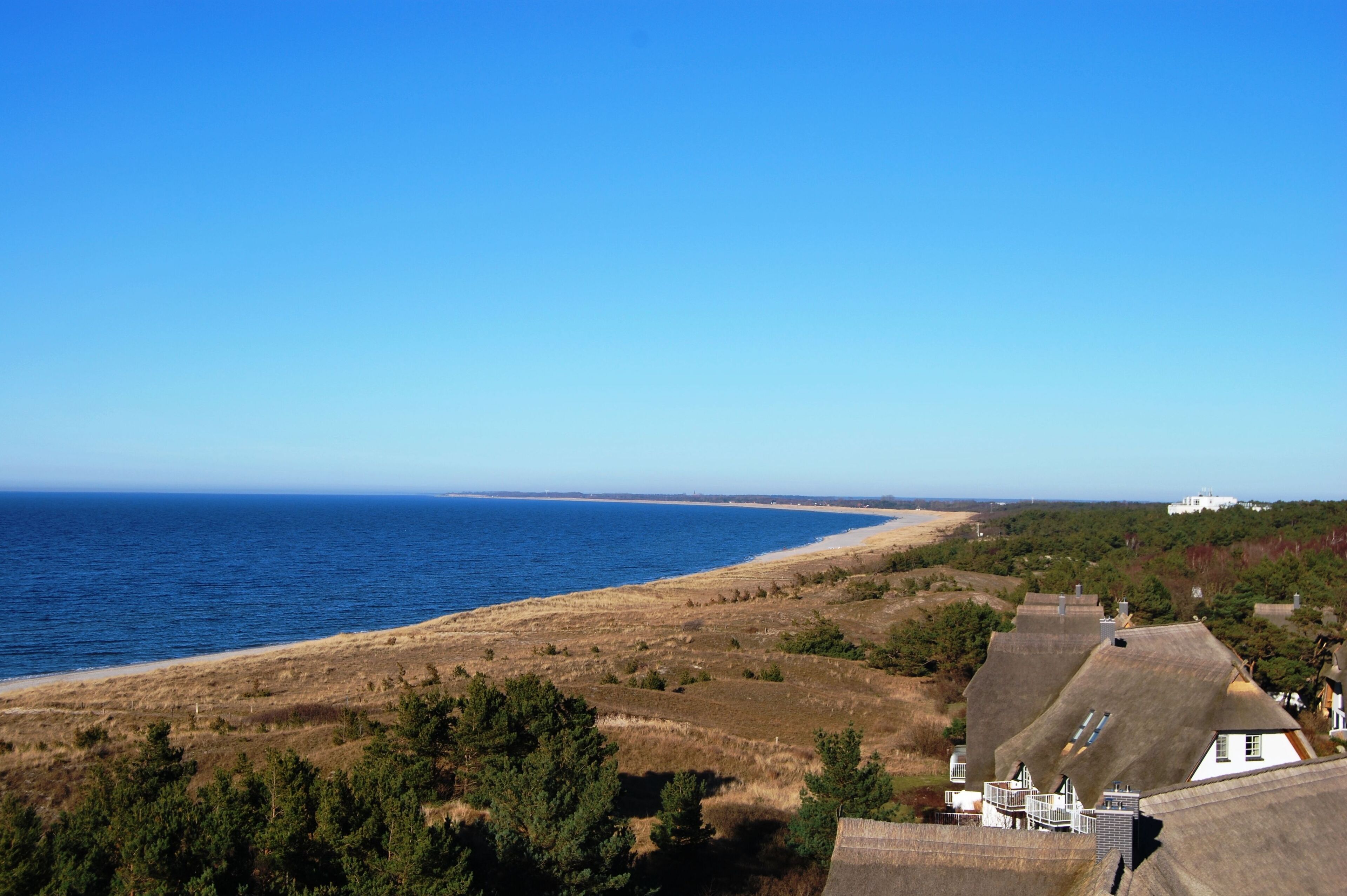 Eine Küstenlandschaft mit Strand, grüner Wiese und einem weißen Gebäude mit geneigtem Dach.