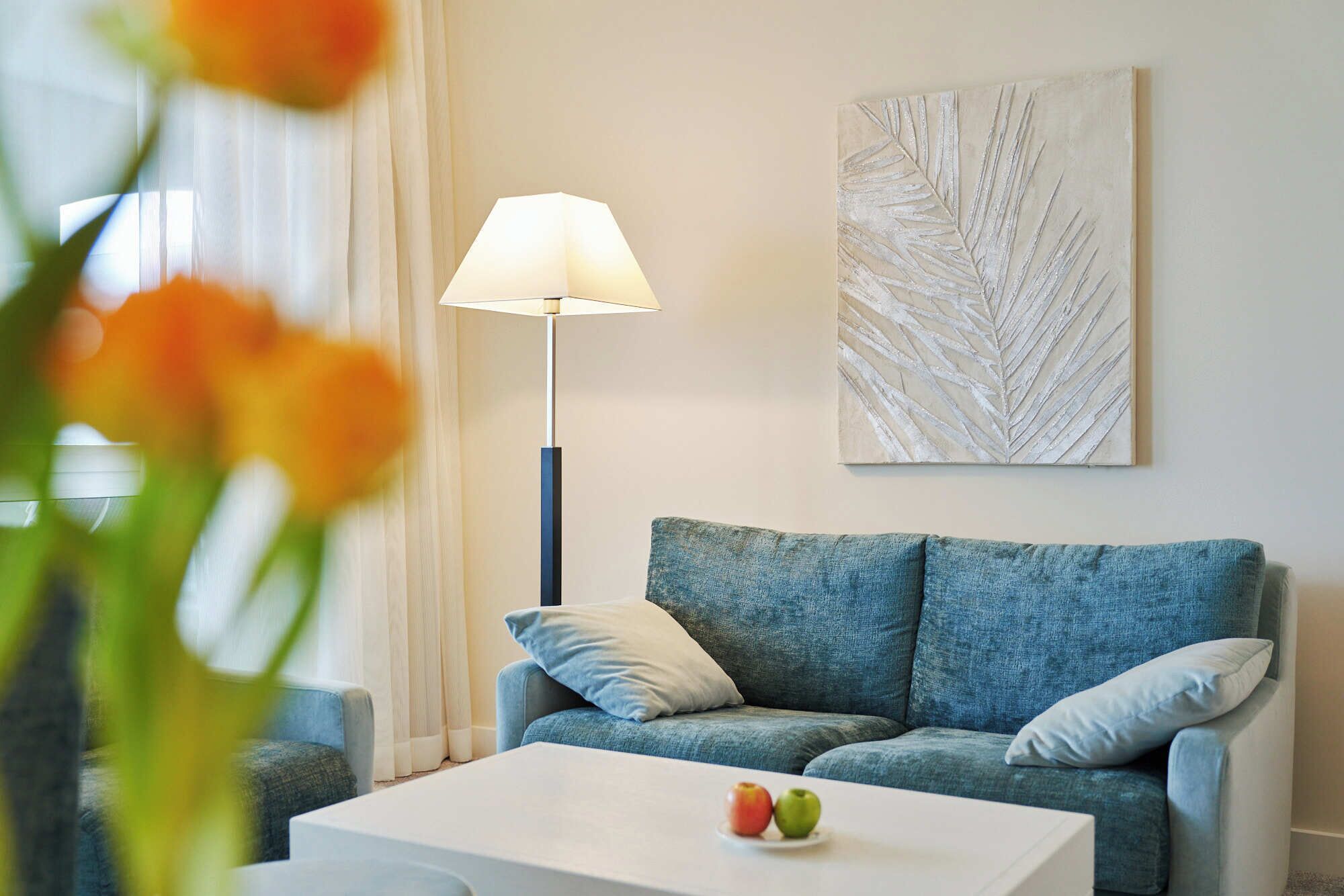 A living room with a blue sofa, a white coffee table, a floor lamp, and a wall art piece.