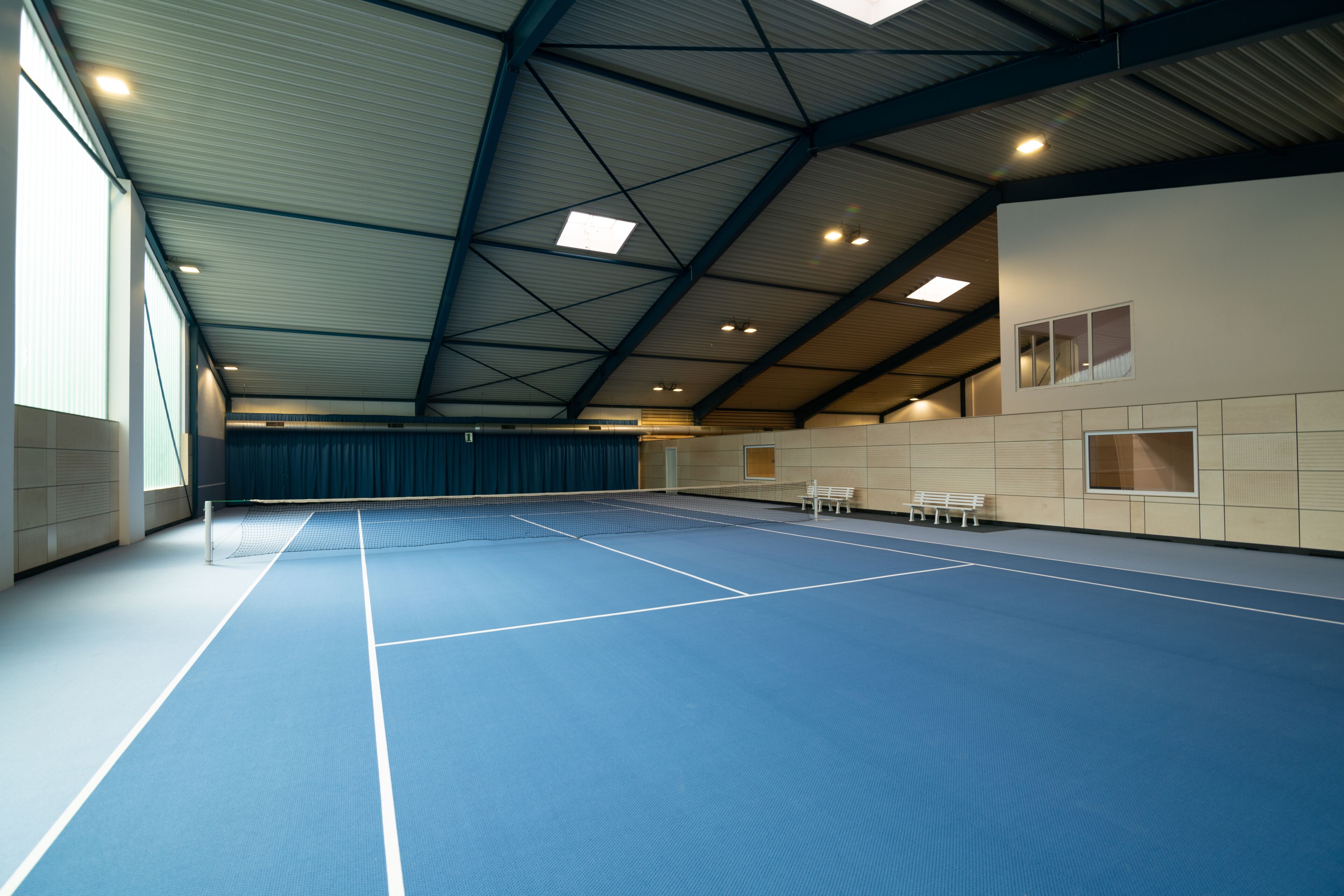 Un court de tennis intérieur doté d’un plafond haut et d’un espace pour les spectateurs.