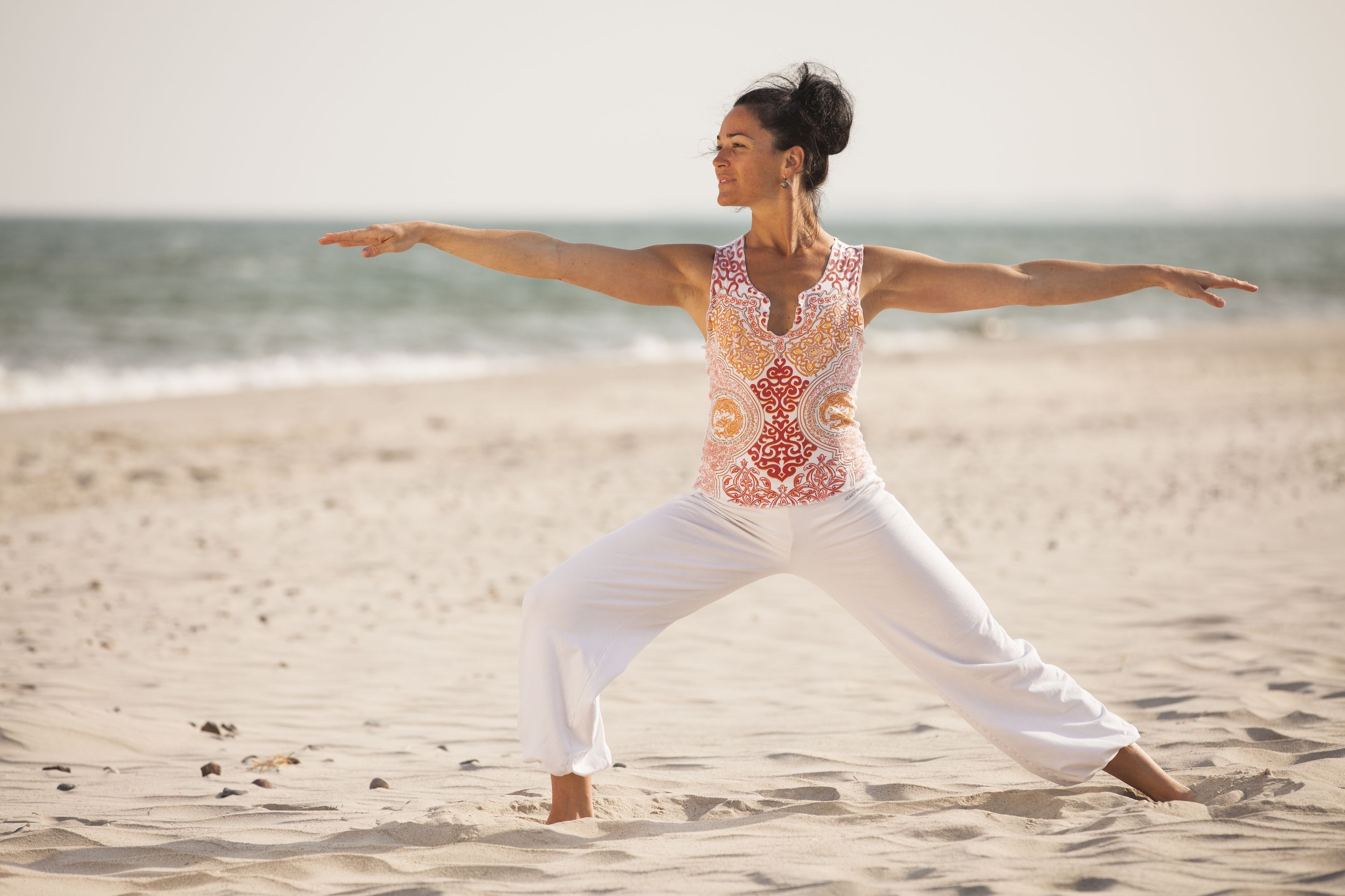 A person performing a yoga pose on a sandy beach with the ocean in the background.
