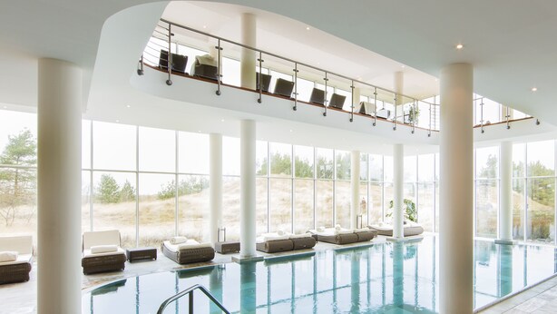 Une grande piscine intérieure dotée de plusieurs espaces de détente et d’une balustrade en verre.