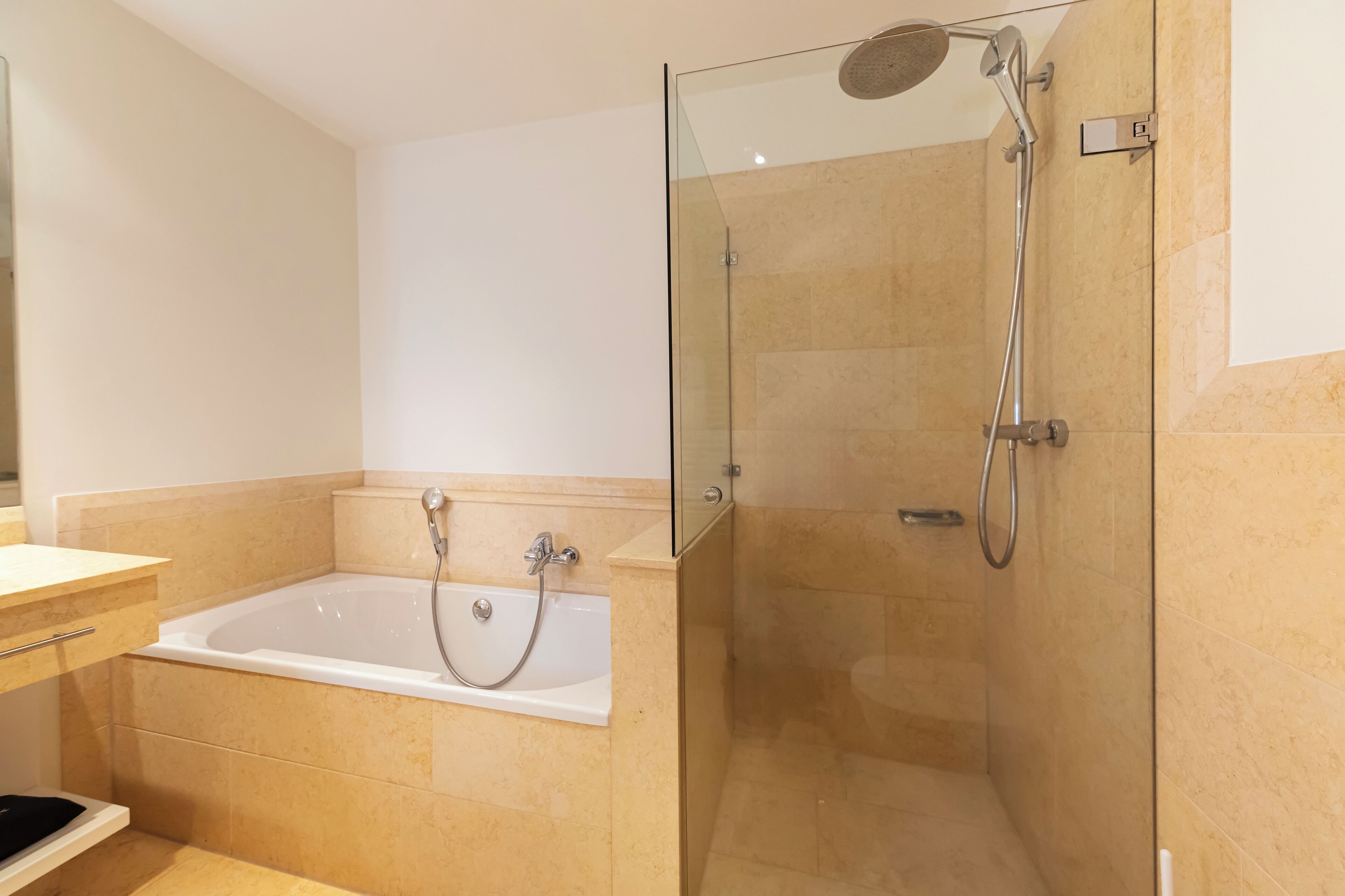 A modern bathroom with a glass-enclosed shower, a standalone bathtub, and beige tiled walls.