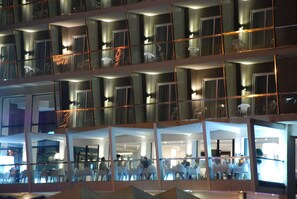 A multi-story hotel with balconies, glass railings, and interior lighting.