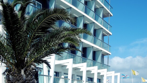 Ein modernes Hotel mit Glasfassade, Balkonen und einer Palme im Vordergrund.