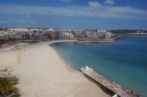 A coastal town with a sandy beach, a calm sea, and a row of buildings along the shore.