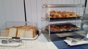 A breakfast buffet with bread and pastries in clear containers.