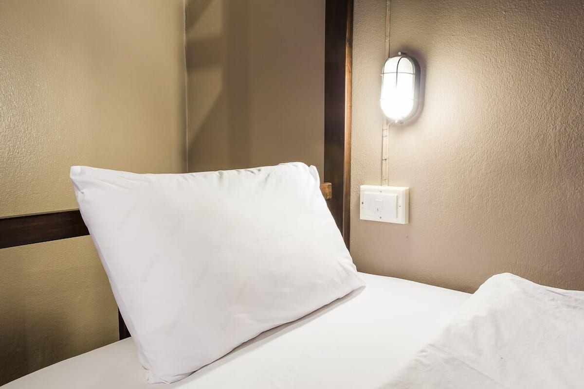 A hotel room with a neatly made bed, a wall-mounted light fixture, and a power outlet.