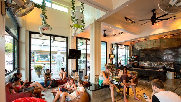 Een ruime lounge met zitmogelijkheden zoals zitzakken en stoelen, een bar met een counter, en grote ramen met uitzicht op de straat.