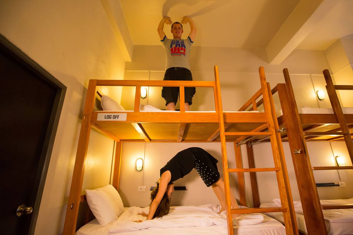 A bunk bed room with a ladder, a bed with a pillow, and a wall-mounted light fixture.