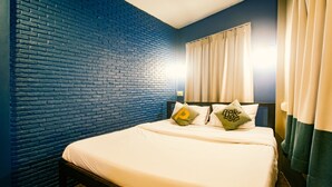 Een hotelkamer met een metselwerkachtergrond, een bed met witte beddengoed en twee kussens met een logo.