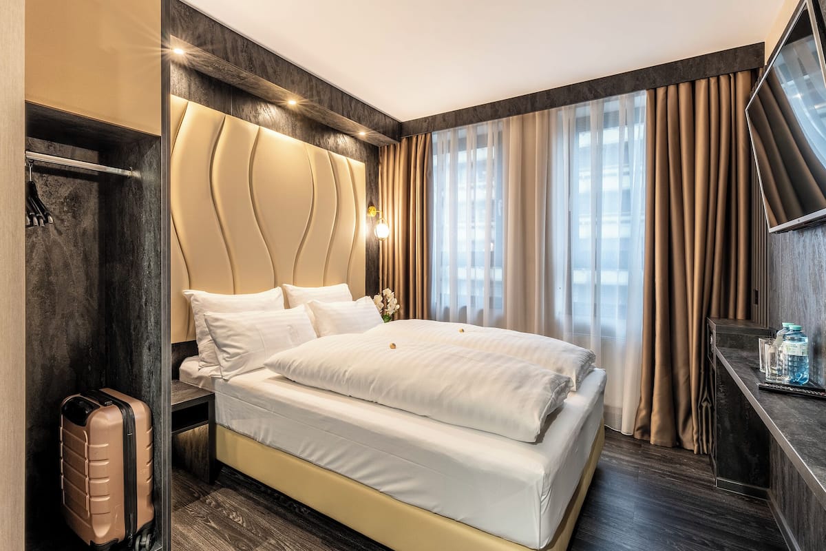 Une chambre d’hôtel moderne avec un grand lit, une table de chevet, un miroir et une vue sur la ville par la fenêtre.