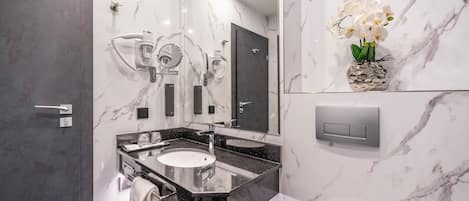 A modern bathroom with a marble wall, a large mirror, a sink, and a vanity with a towel rack.