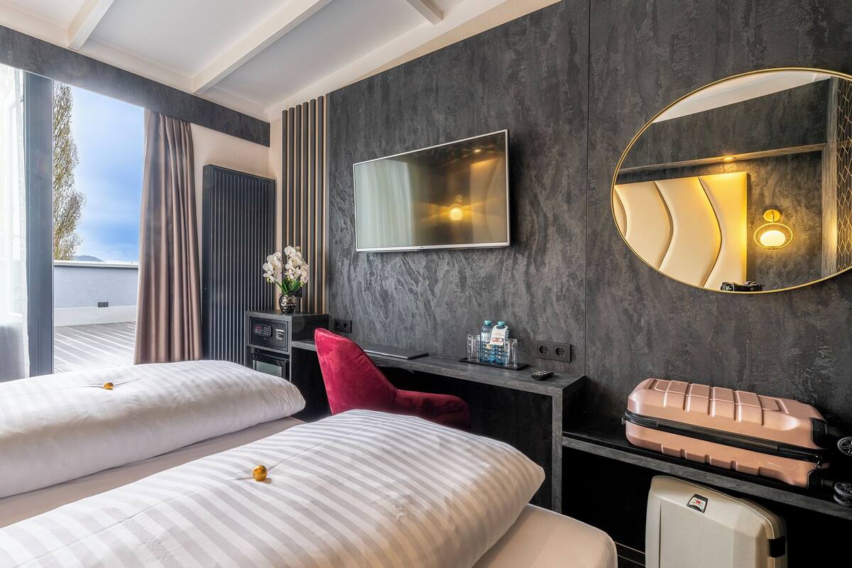 Une chambre d’hôtel avec deux lits, une télévision, un miroir, un bureau avec une lampe et une valise.