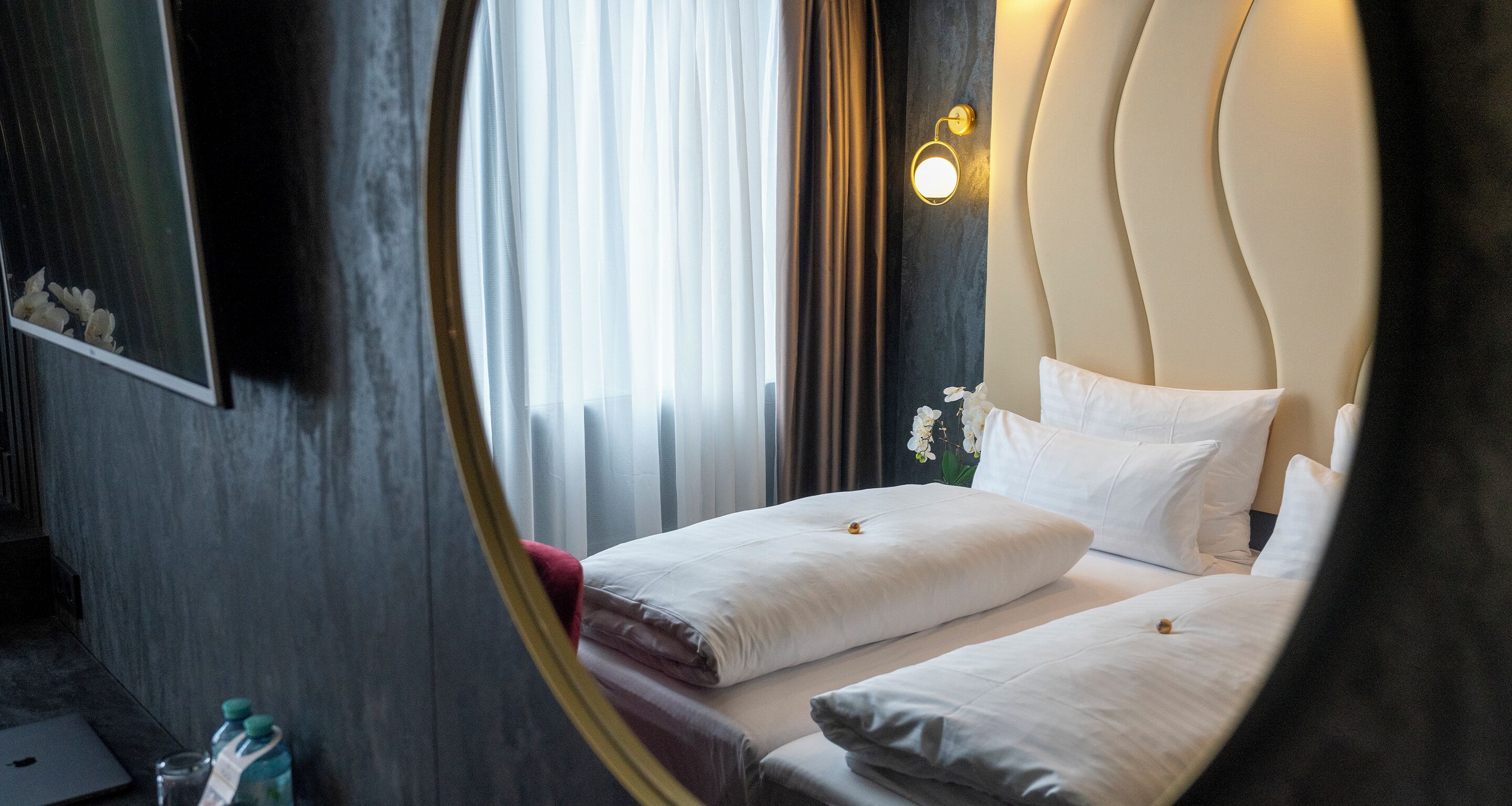 Ein Hotelzimmer mit einem Bett, einem Spiegel, einem Laptop und einer Wasserflasche.