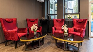 A room with four red velvet chairs around a glass table with a yellow rim, a vase with white flowers, and a view of buildings through large windows. - PLAZA INN Salzburg City (Salzburg)