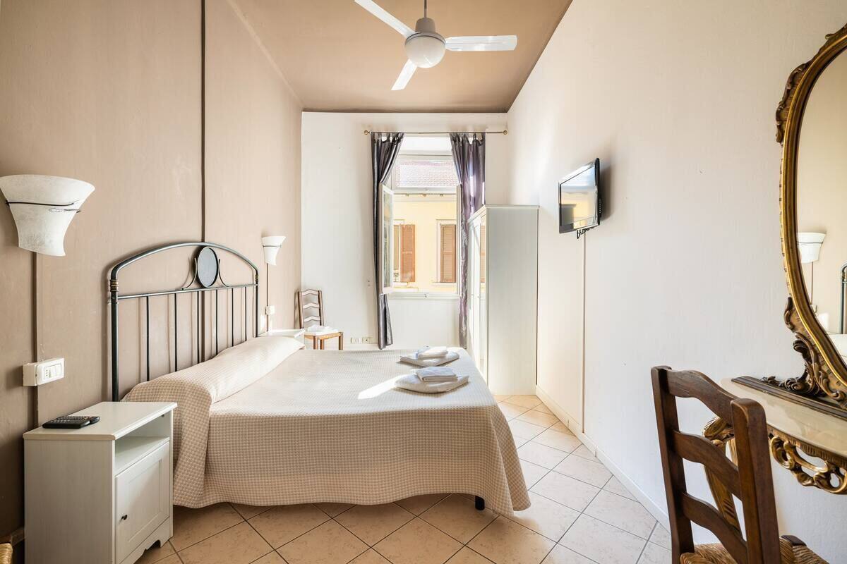 A hotel room with a bed, bedside table, lamp, mirror, and a view of the outside.