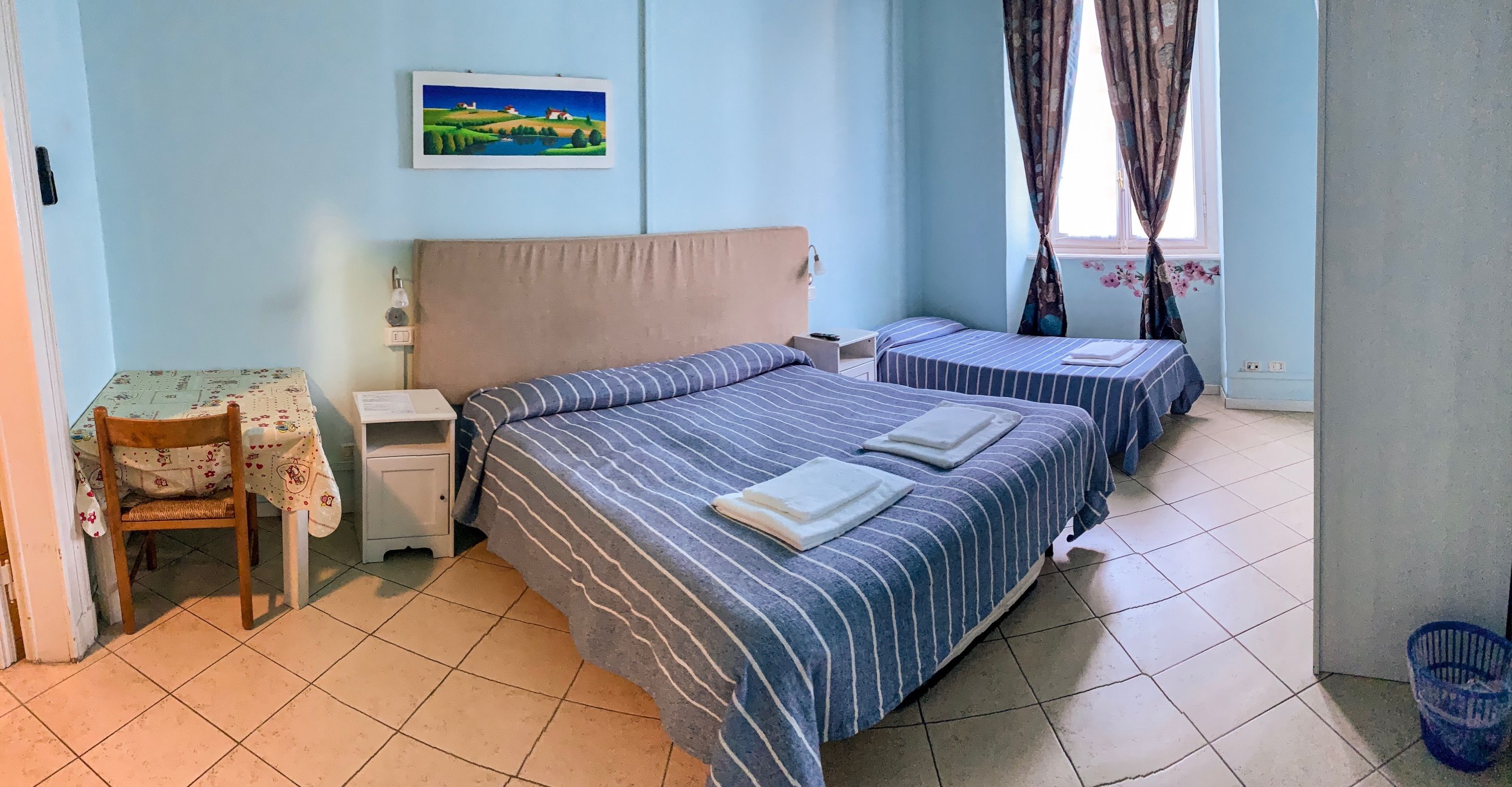 Een slaapkamer met twee bedden, een nachtkastje, een stoel en een schilderij aan de muur.