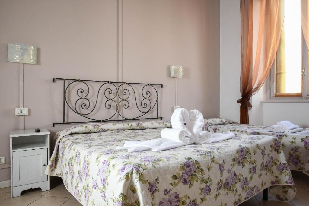 A bedroom with two beds, a nightstand, a wall-mounted lamp, and a window with curtains.