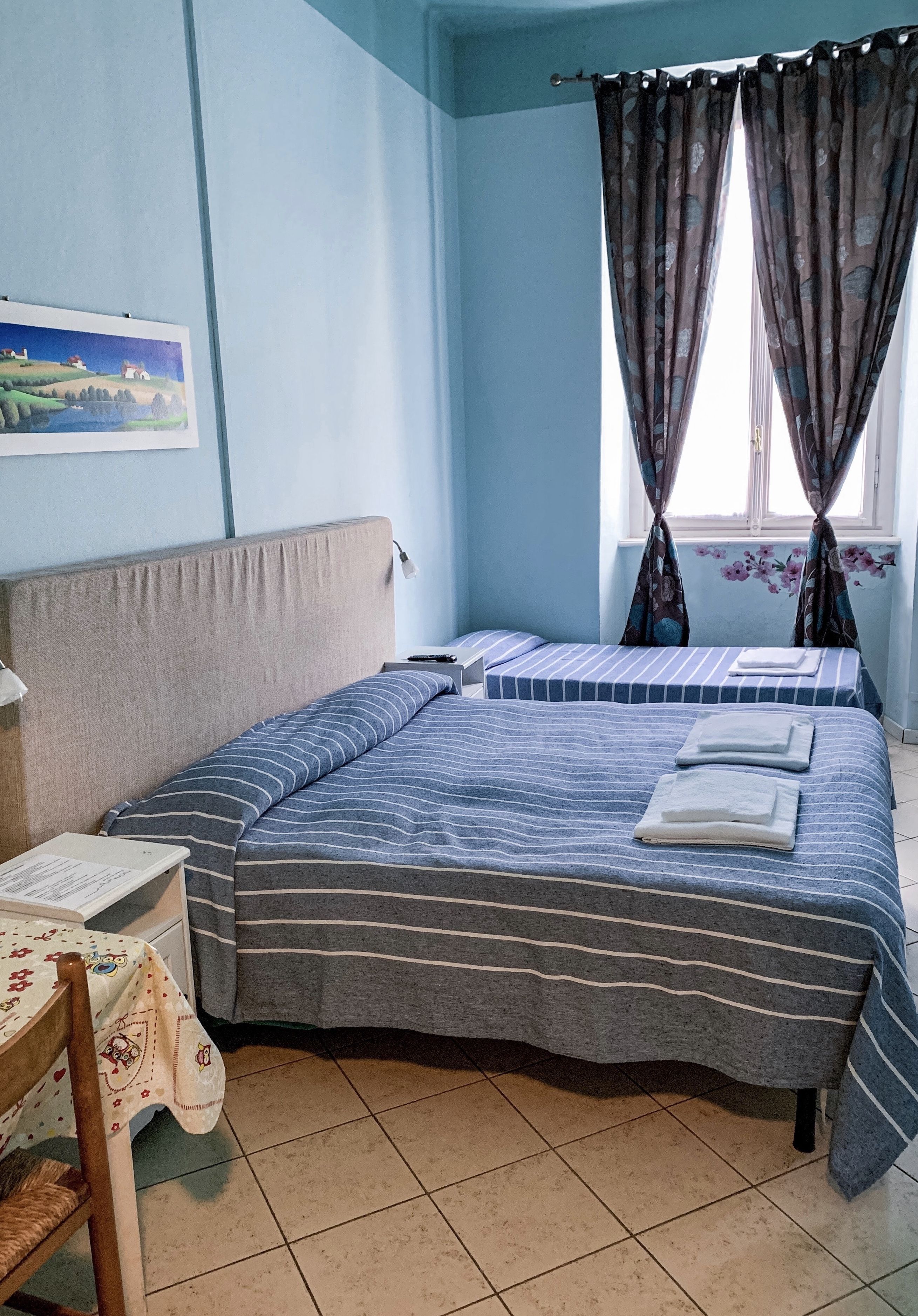 A bedroom with two beds, a table, and a chair.