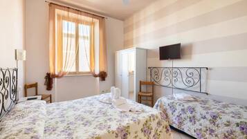 Quarto com duas camas, um guarda-roupa, uma televisão e uma janela com cortinas.