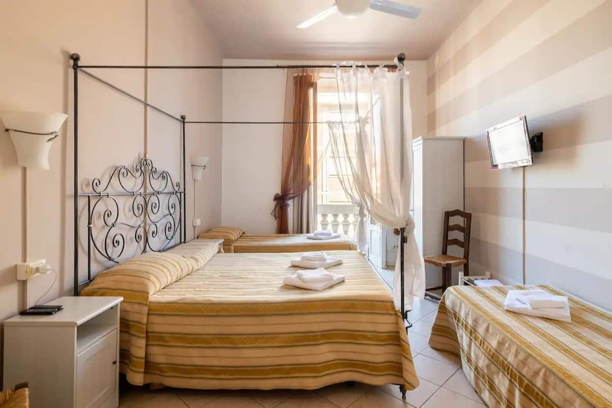 A hotel room with two beds, a desk, a chair, a TV, and a balcony with curtains.