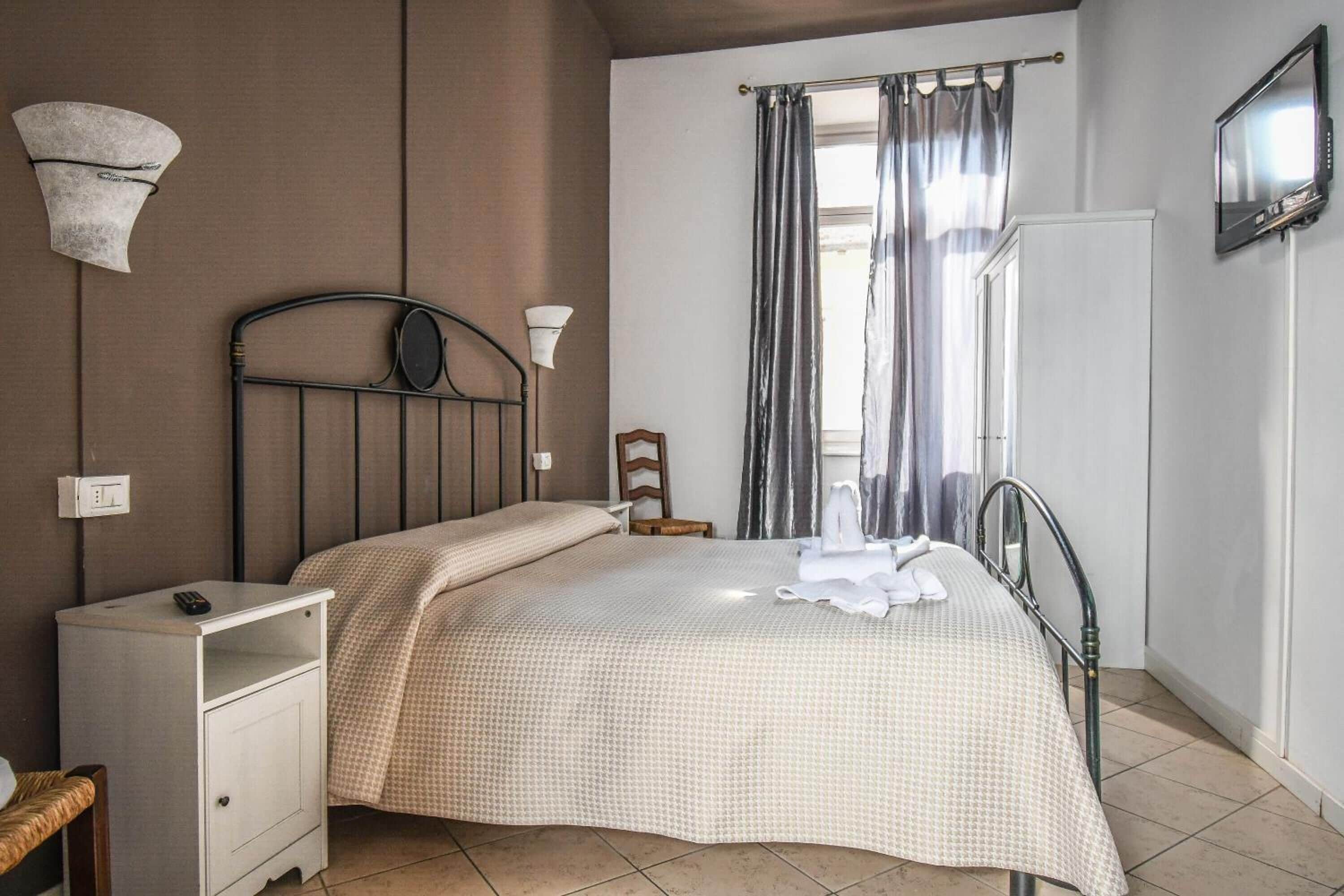 A bedroom with a bed, bedside table, lamp, and a television on the wall.