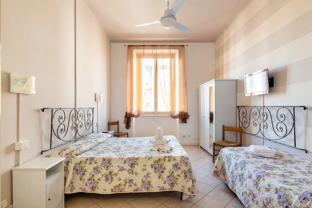 A bedroom with two beds, a wardrobe, a television, and a ceiling fan.
