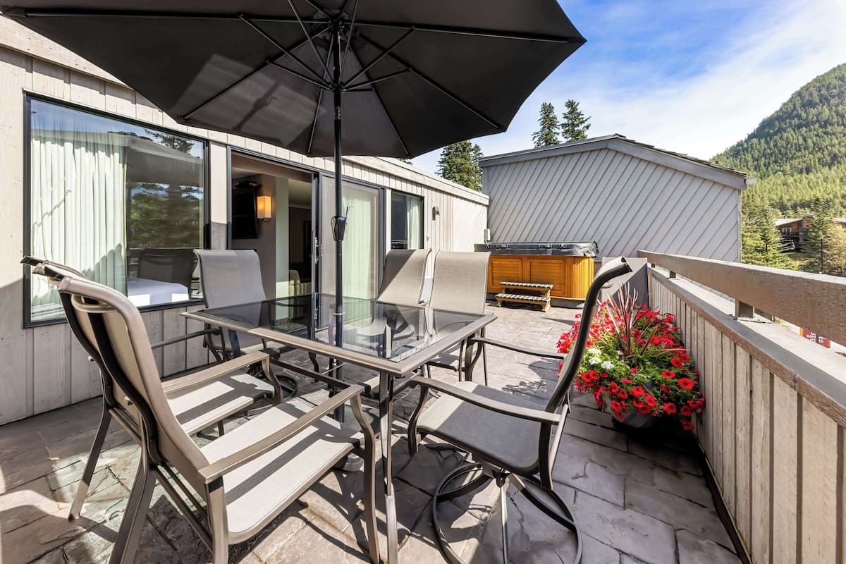 An outdoor patio with a glass table and chairs, an umbrella, and a view of a mountain.