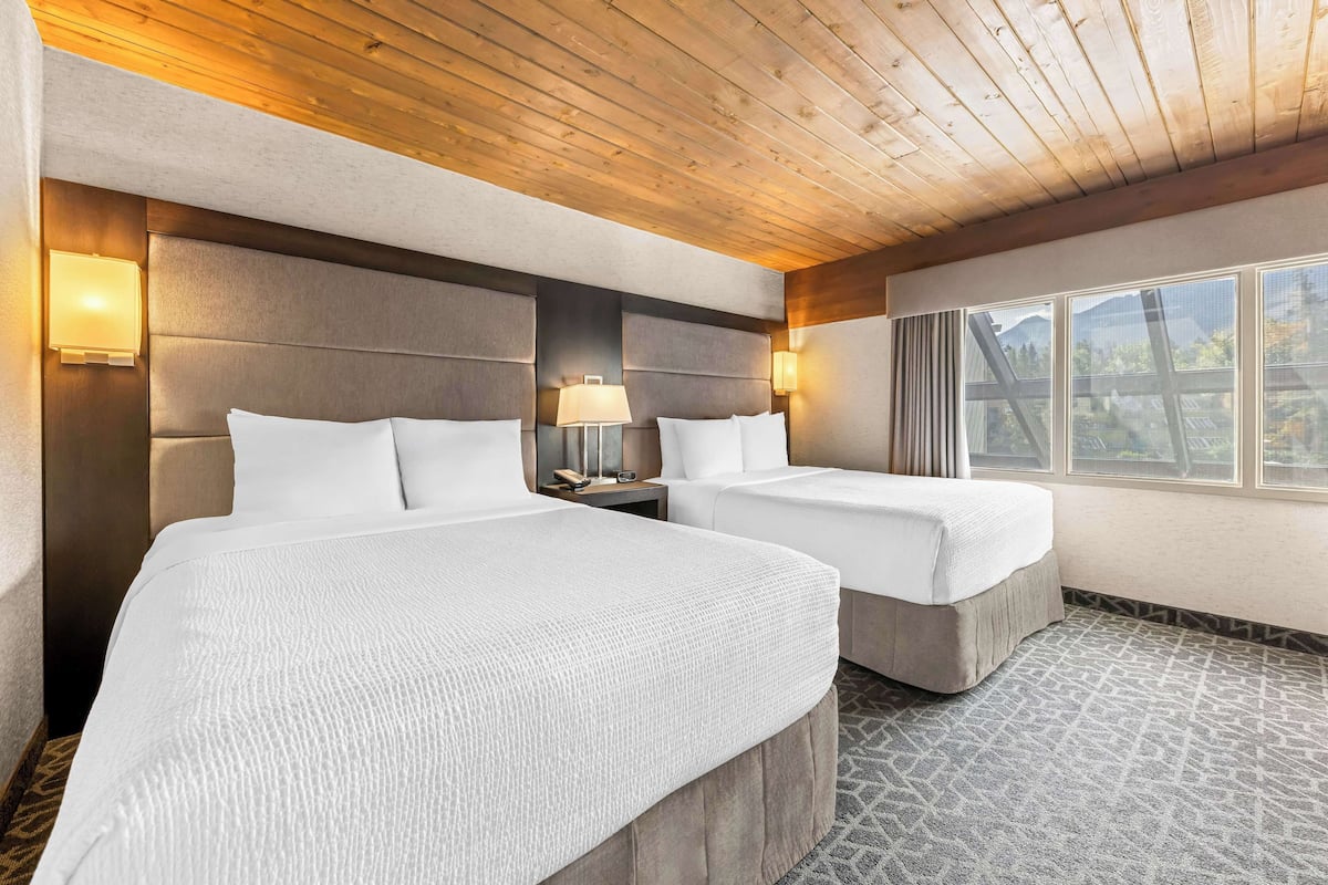 A hotel room with two beds, wooden ceiling, and a large window with a view.