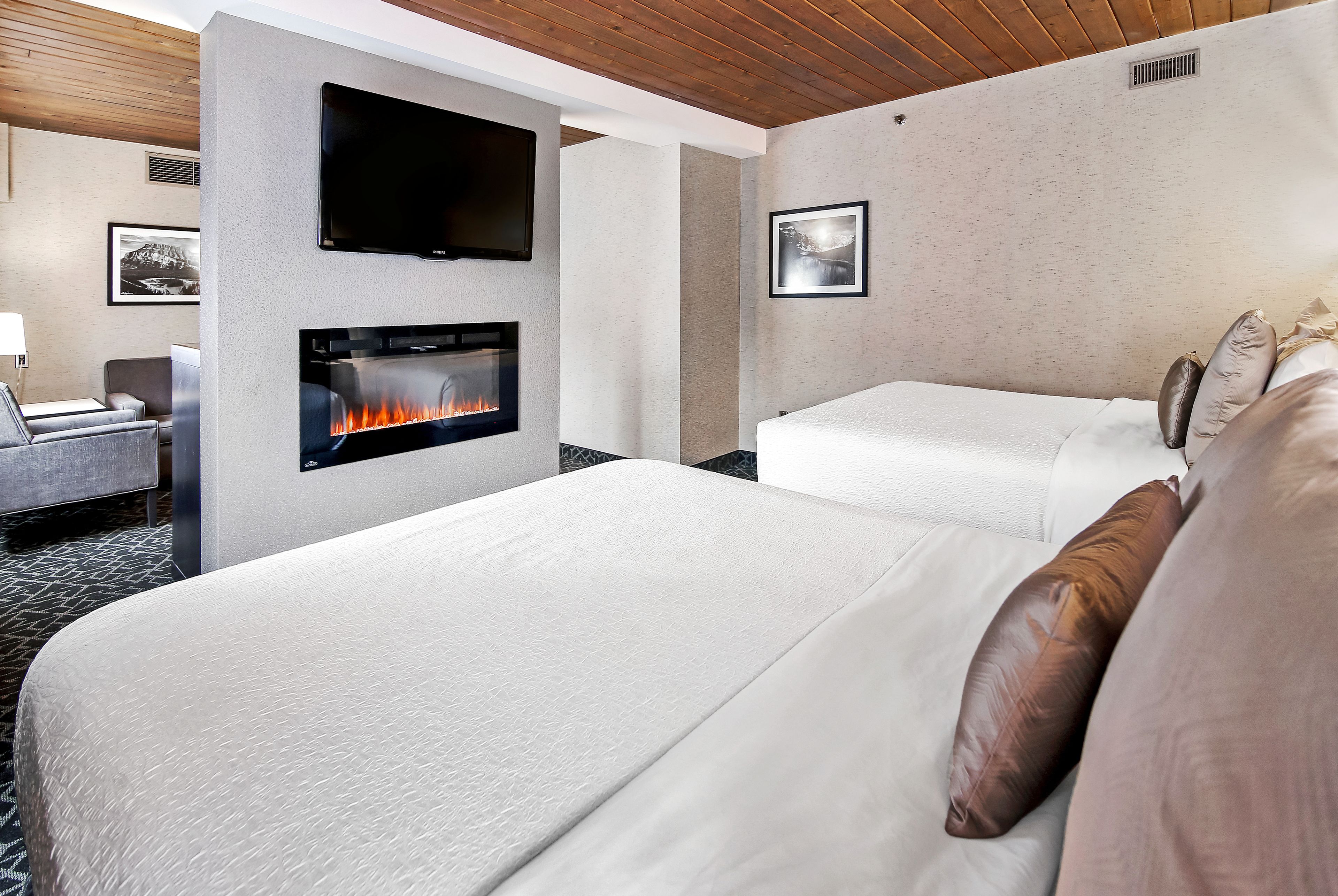 A hotel room with a fireplace, a TV mounted on the wall, and two beds.