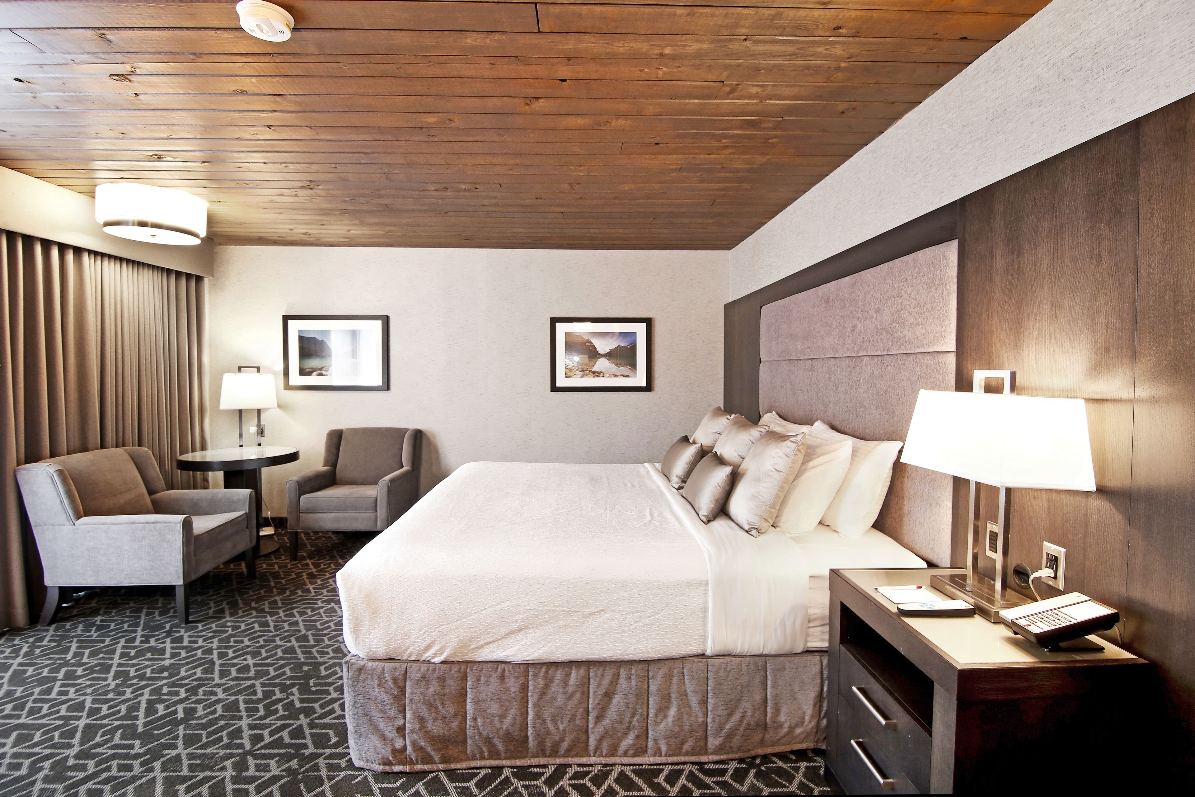 Een hotelkamer met een groot bed, twee fauteuils, een kleine tafel en een nachtkastje met een lamp en telefoon.