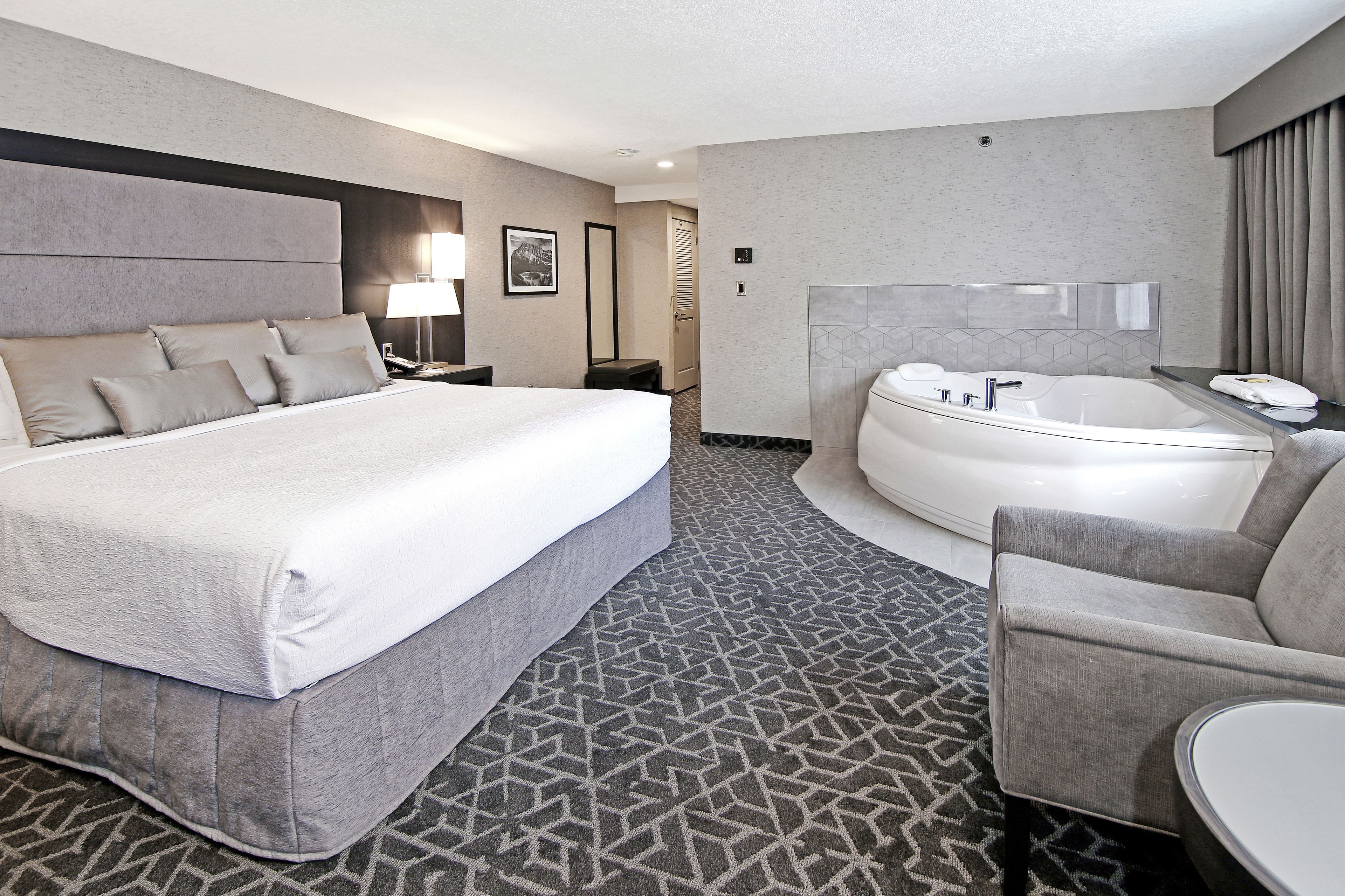 Habitación de hotel con una cama grande, una zona de estar separada, una bañera y una pequeña mesa.