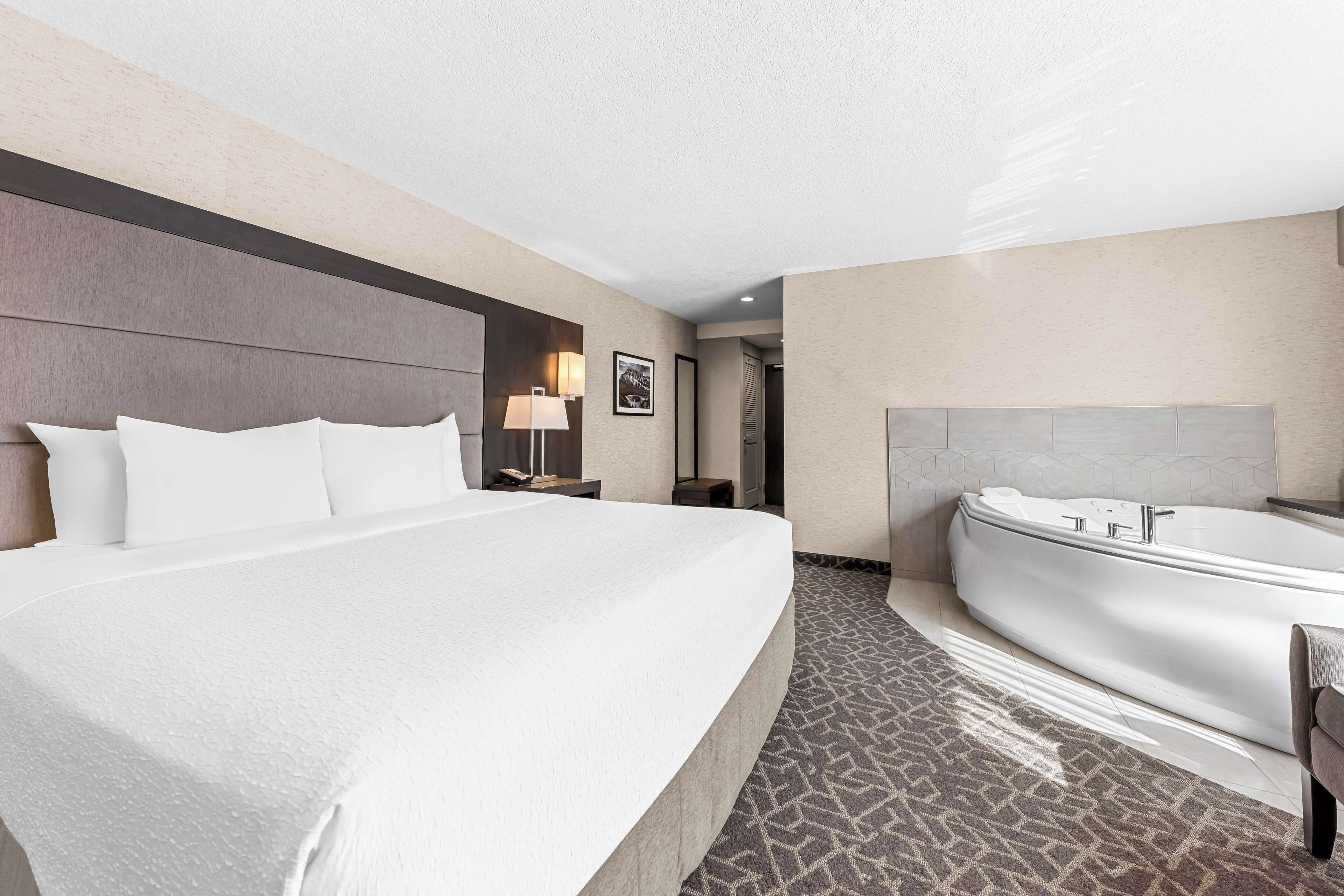 A hotel room with a large bed, a separate bathroom with a bathtub, and a small table with a lamp.