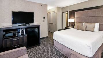 A hotel room with a bed, a TV, a desk with a lamp, and a minibar.