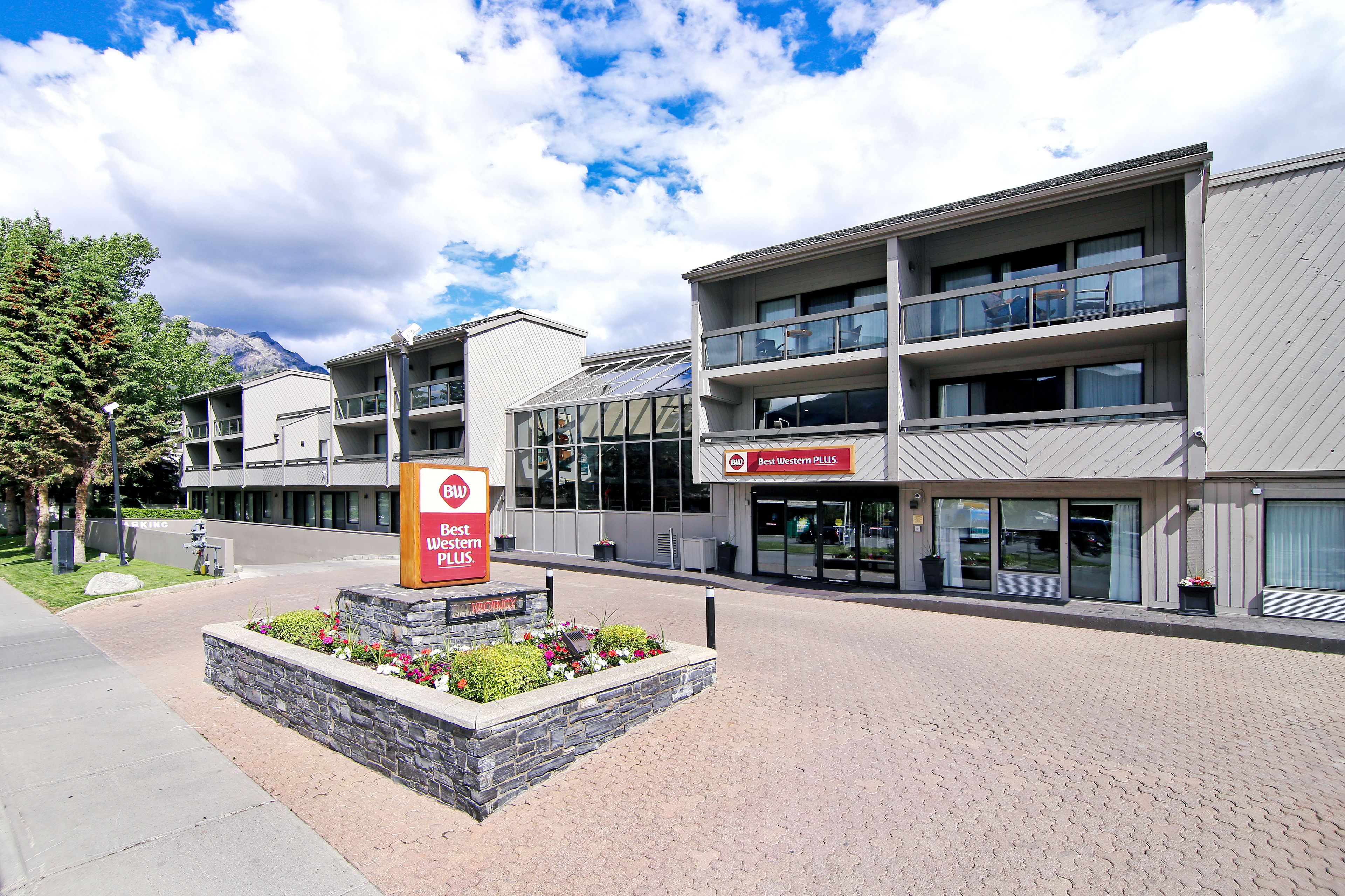 A multi-story hotel with a modern design, featuring a landscaped area with flowers and a sign for Best Western PLUS.