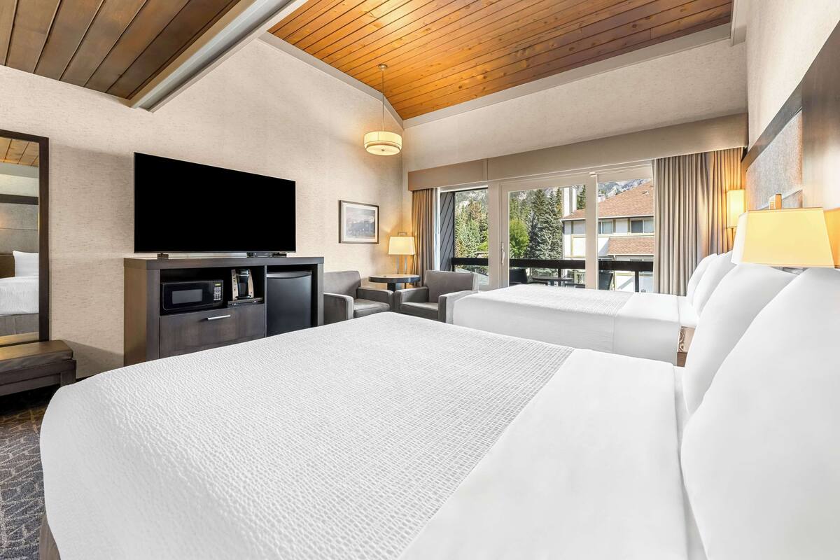 A hotel room with a large bed, a TV, a desk with a microwave, and a view of the outdoors.