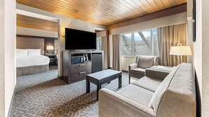 Une chambre d’hôtel comprenant un lit, une télévision, une petite kitchenette, un canapé et un balcon avec des rideaux.