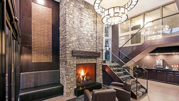 Un intérieur moderne avec une cheminée en pierre, un coin salon et un escalier menant à la cuisine.