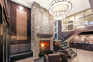 Un intérieur moderne avec une cheminée en pierre, un coin salon et un escalier menant à la cuisine.