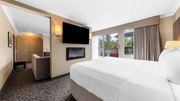 Een hotelkamer met een groot bed, een flatscreen televisie aan de muur, een zithoek met een fauteuil en uitzicht door het raam.
