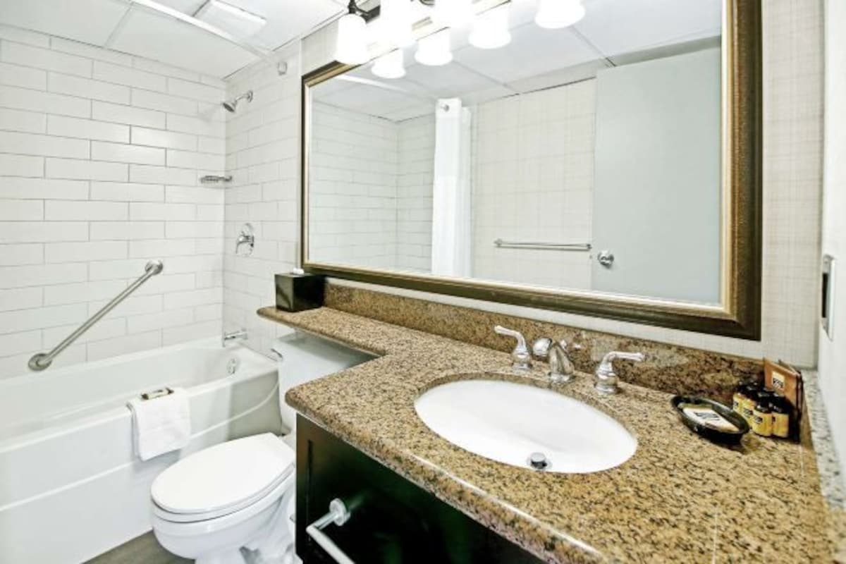 A bathroom with a white bathtub, a white toilet, a granite countertop sink, and a large mirror.