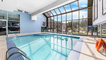 A swimming pool with clear blue water, surrounded by tiled flooring and metal railings.